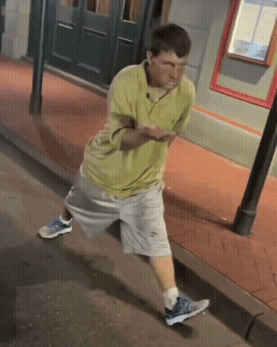 Man In Yellow Shirt And Grey Shorts On Sidewalk GIF