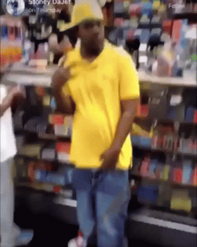 Man In Yellow Shirt And Hat Standing In Front Of Store GIF