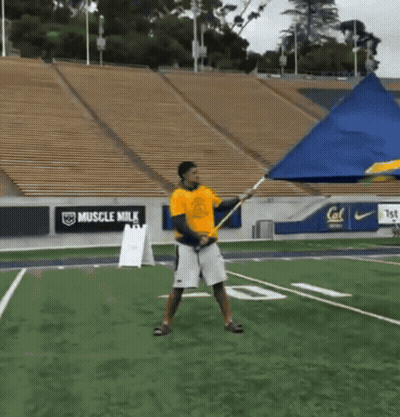 Man In Yellow Shirt Holding Flag With Muscle Milk Ads GIF