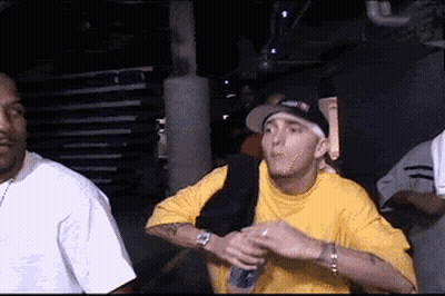 Man In Yellow Shirt Holding Microphone Next To Man In Black Hat GIF
