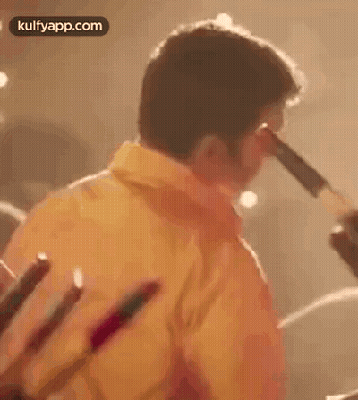 Man In Yellow Shirt Holding Sticks GIF