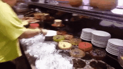 Man In Yellow Shirt In Front Of Cakes And Plates GIF