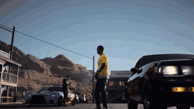 Man In Yellow Shirt Next To Black Car In Front Of Holiday Building GIF
