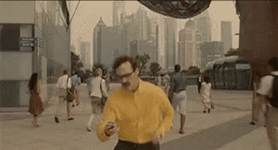 Man In Yellow Shirt Running Looking At Cell Phone GIF