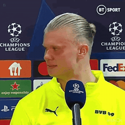 Man In Yellow Shirt Talking Into Microphone In Front Of Champions League Sign GIF