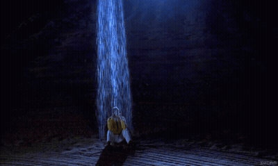 Man In Yellow Shirt Under Waterfall In Dark Room GIF