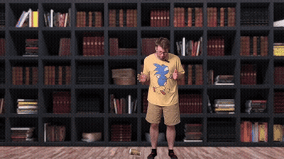 Man In Yellow Shirt With Blue Sonic In Front Of Bookshelf GIF