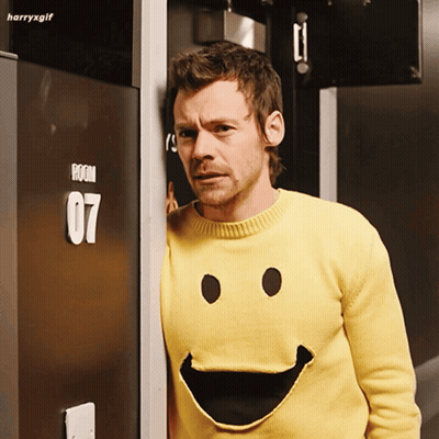 Man In Yellow Smiley Sweater In Front Of Room 07 Door GIF