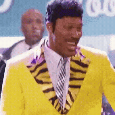 Man in Yellow Suit and Tie Smiling in Front of Crowd