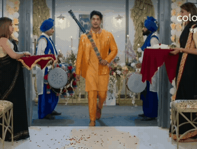 Man In Yellow Suit Walking Through Doorway Surrounded By Blue Turbans GIF