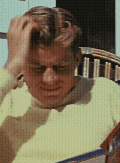 Man In Yellow Sweater Scratching Head Reading Magazine GIF