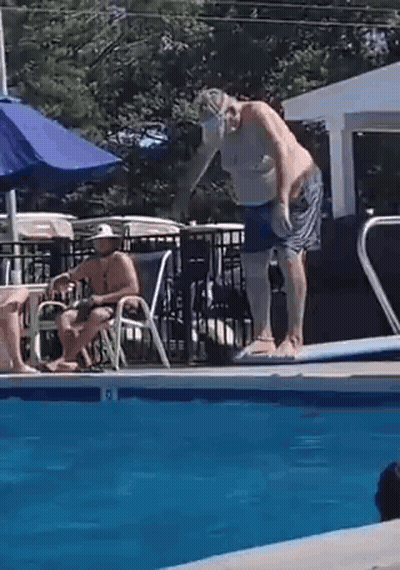 Man Jumping Into Pool While Another Sits On Chair GIF