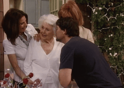 Man Kissing Older Woman On Cheek In Front Of Two Women GIF