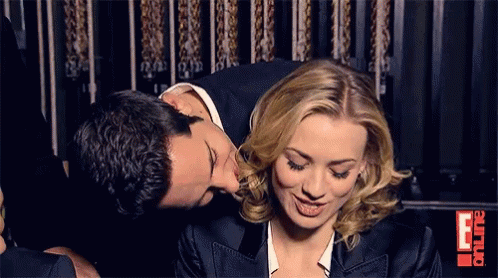 Man Kissing Woman On Cheek In Front Of E Sign GIF
