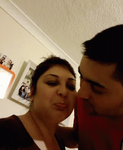 Man Kissing Woman On Cheek In Front Of Pictures GIF