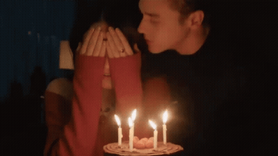 Man Kissing Woman's Cheek Lit Birthday Cake Candles GIF