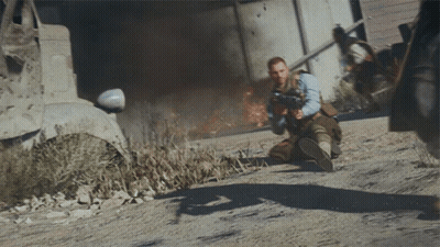 Man Kneeling Holding Gun Before Burning Building GIF