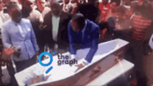 Man Kneeling Over Coffin With Crowd Surrounding GIF