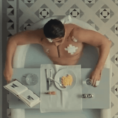 Man Laying In Bathtub With Food And Book GIF