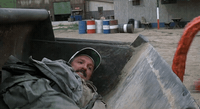 Man Laying In Dumpster With Barrels GIF
