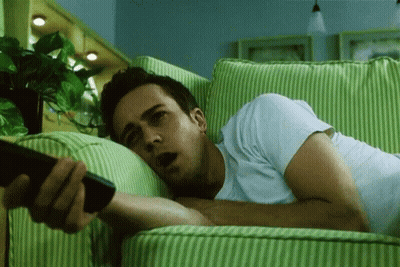 Man Laying On Green And White Striped Couch Holding Remote GIF