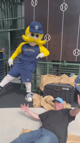 Man Laying On Ground Next To Mascot In Brewers Jersey GIF