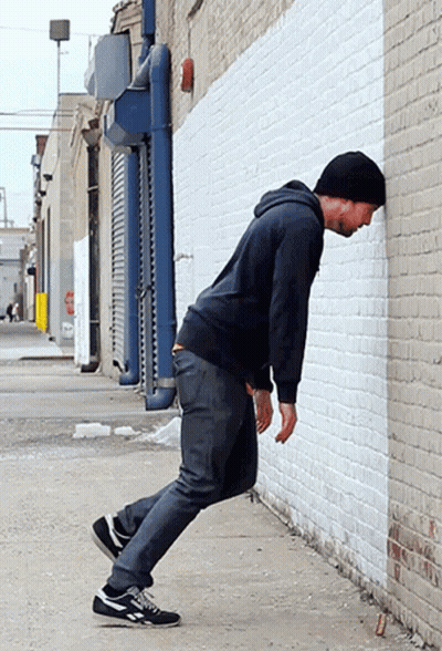 Man Leaning Against White Brick Wall In Alleyway GIF