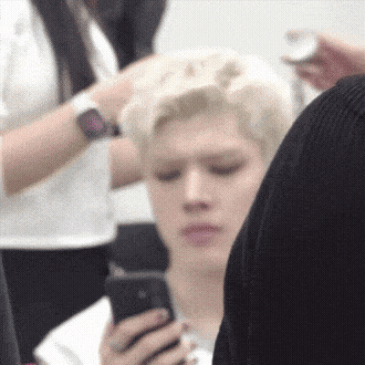 Man Looking At Phone While Another Gets Haircut GIF
