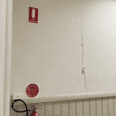 Man Looking Through Hole In Wall With Red Sign Saying Co GIF