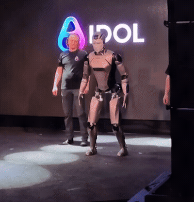 Man Next To Robot In Front Of Idol Sign GIF