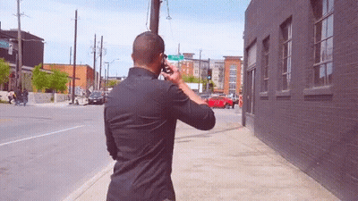Man On Phone Walking By Green Street Sign GIF