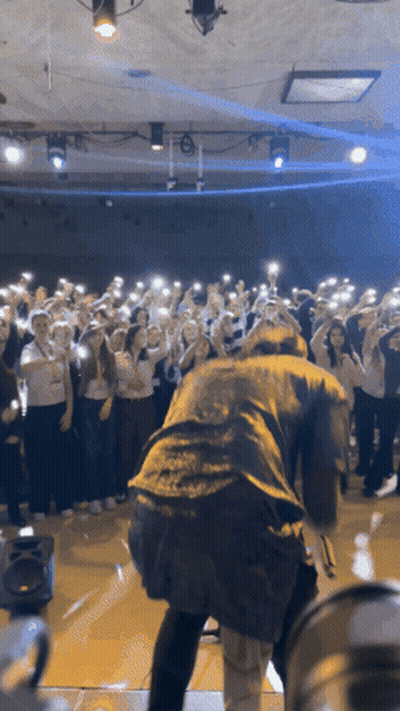 Man On Stage In Front Of Crowd Holding Up Phones GIF