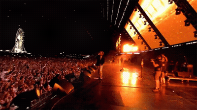 Man On Stage In Front Of Ferris Wheel GIF