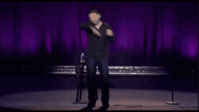 Man On Stage With Microphone In Front Of Purple Curtain GIF