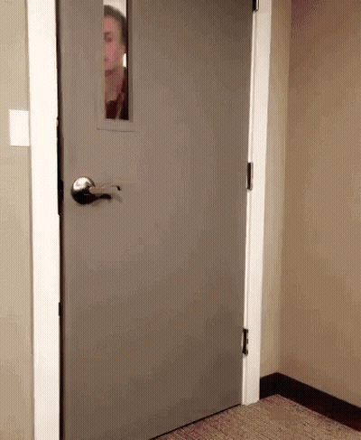 Man Peeking Out Of Gray Door With Window GIF