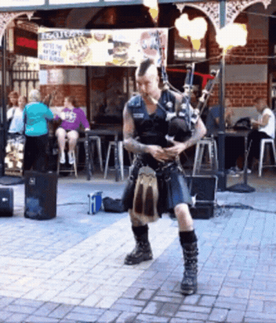 Man Playing Bagpipes In Front Of Scottish Sign GIF