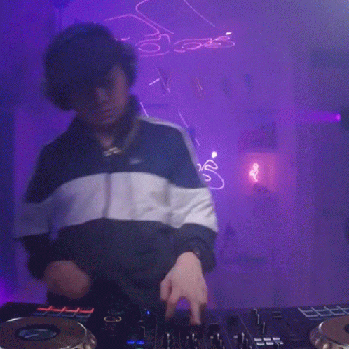 Man Playing DJ Set With Purple Background and Neon S Sign