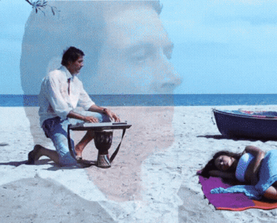 Man Playing Drum On Beach With Woman Laying On Towel GIF