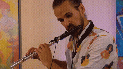 Man Playing Flute In Front Of Colorful Painting GIF
