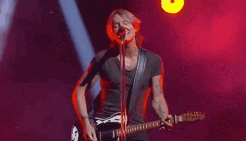 Man Playing Guitar And Singing Into Microphone On Stage GIF
