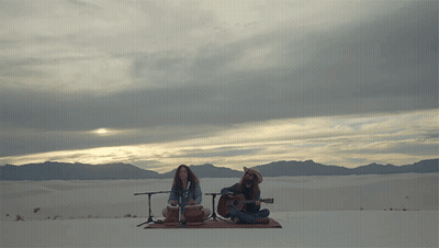 Man Playing Guitar And Woman Playing Drum In Desert GIF