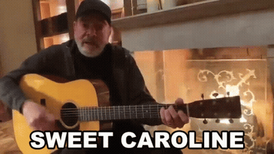 hombre tocando guitarra frente a chimenea diciendo Sweet Caroline GIF