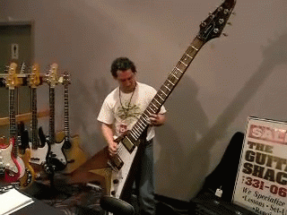 Man Playing Guitar in Front of Guitar Shack Sign
