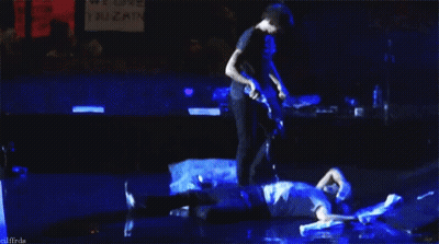 Man Playing Guitar While Another Man Laying On Stage GIF