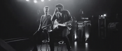 Man Playing Guitar While Another Sits On Bar Stool GIF