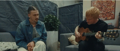 Man Playing Guitar While Another Sits On Couch GIF