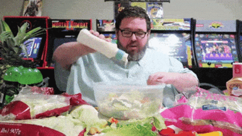 Man Pouring Dressing Into Salad In Front Of Mortal Kombat Arcade GIF