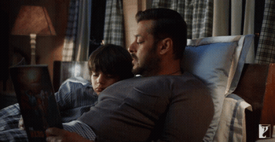 Man Reading Book To Boy Lying On Stomach GIF