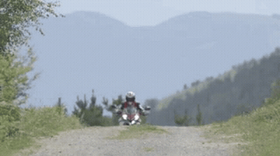 Man Riding Motorcycle On Dirt Road With Mountains GIF