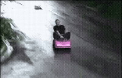 Man Riding Pink Sled Down Flooded Street GIF